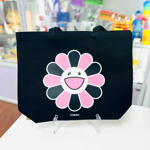 Bolso tote negro con motivos coloridos de flores sonrientes y logotipos de BLACKPINK, una colaboración de Takashi Murakami.