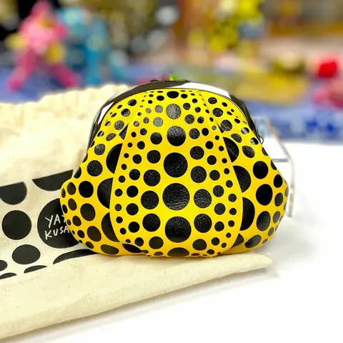 Bolso Calabaza Gamaguchi de Yayoi Kusama, naranja con puntos negros, sobre un fondo blanco.