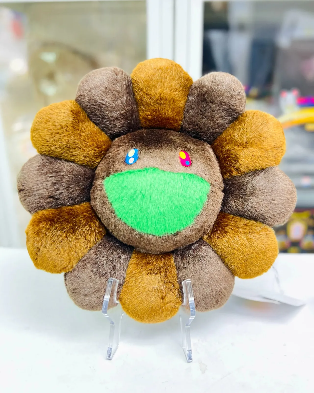 Cojín de flor sonriente de Takashi Murakami en color marrón, sobre un fondo neutro.