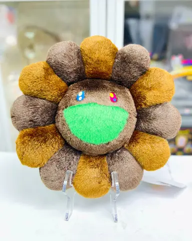 Cojín de flor sonriente de Takashi Murakami en color marrón, sobre un fondo neutro.
