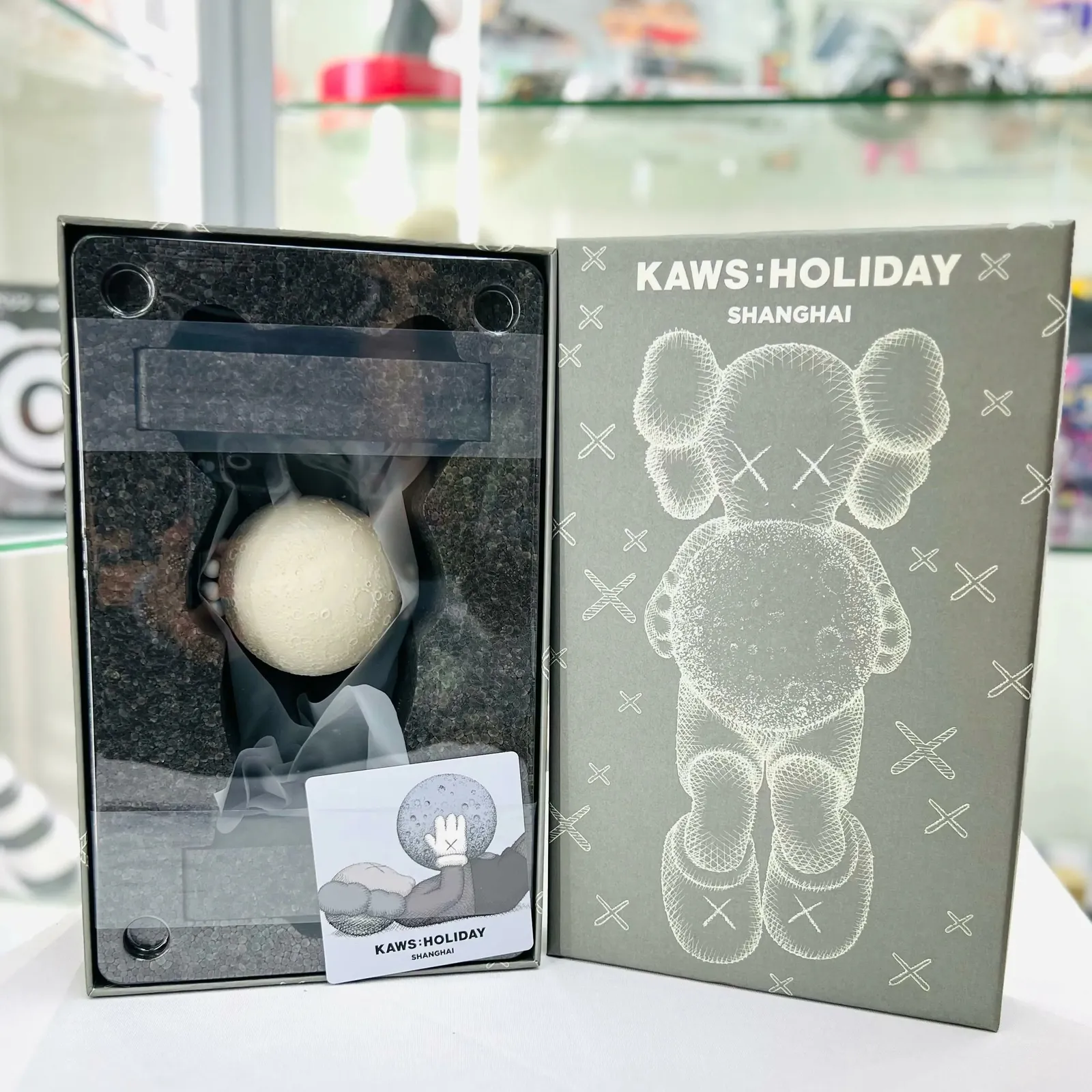 KAWS:HOLIDAY SHANGHAI grey vinyl figure with moon element, placed on a neutral surface.